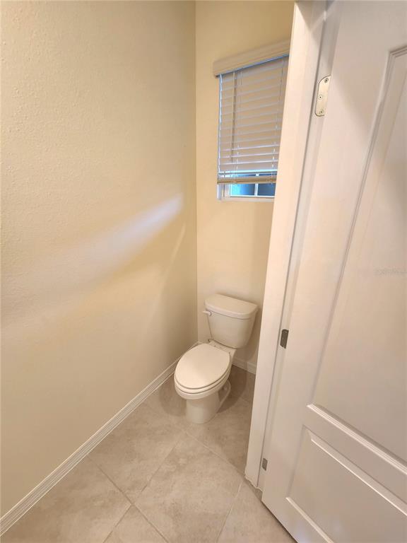 A small bathroom features a white toilet, tiled flooring, and a window with blinds — 1141 BLUE JAY DRIVE, DAVENPORT, FL