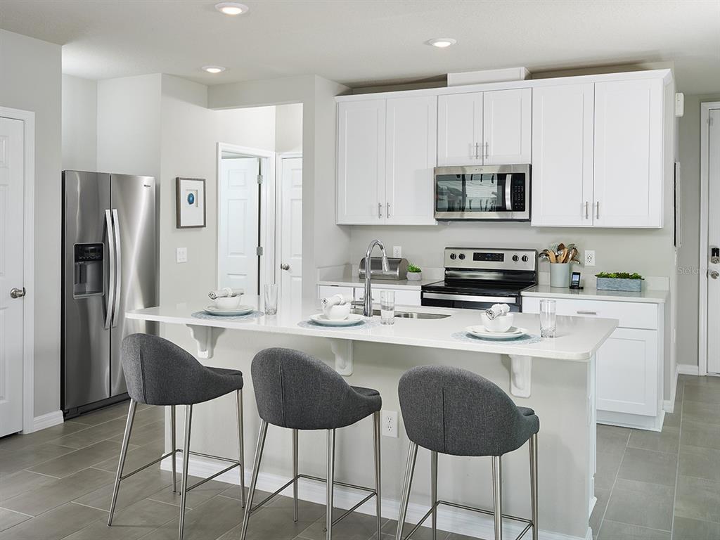 A modern kitchen features white cabinets, stainless steel appliances, a quartz island, and gray stools — 4540 BURROWING OWL LOOP, ST CLOUD, FL