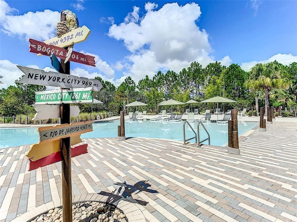 A wooden signpost with city distances stands on a paved deck beside a swimming pool — 840 BENOI DR DRIVE, DAVENPORT, FL
