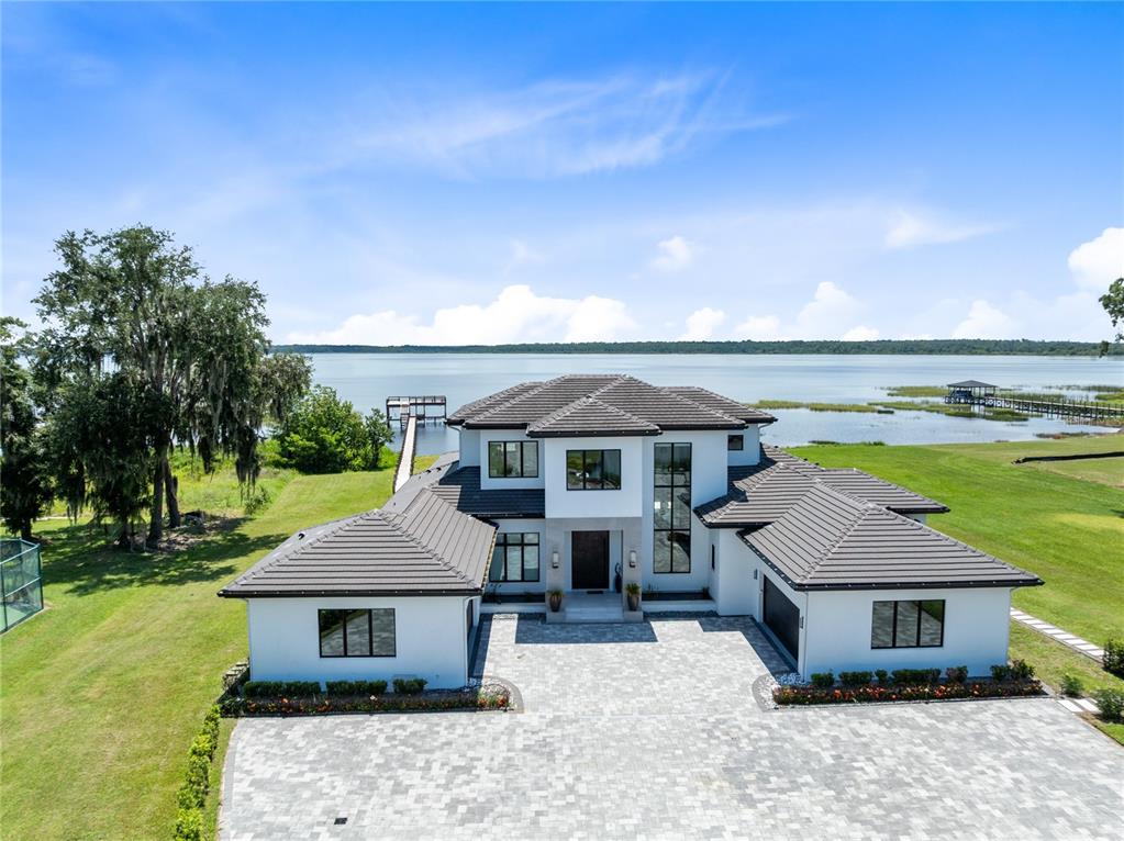 An aerial view of a modern white house with a dark roof beside a lake — 13395 KIRBY SMITH ROAD, ORLANDO, FL