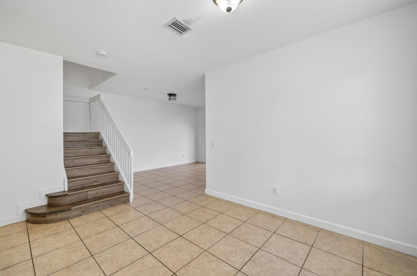 A room with beige tile flooring, white walls, and a staircase with wood-look steps — 7029 Ambrosia Lane # 606, Naples FL 34119, NAPLES, FL