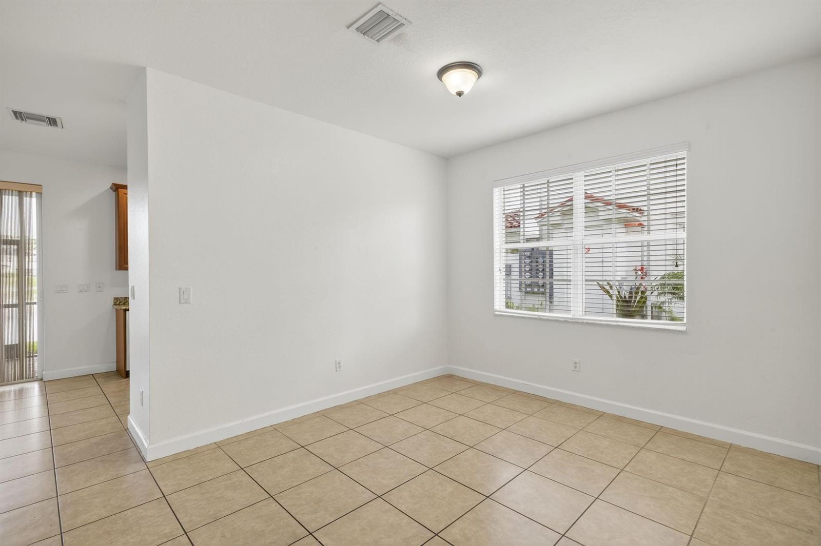 An empty dining area with beige tile floors, white walls, and a window with blinds — 7029 Ambrosia Lane # 606, Naples FL 34119, NAPLES, FL