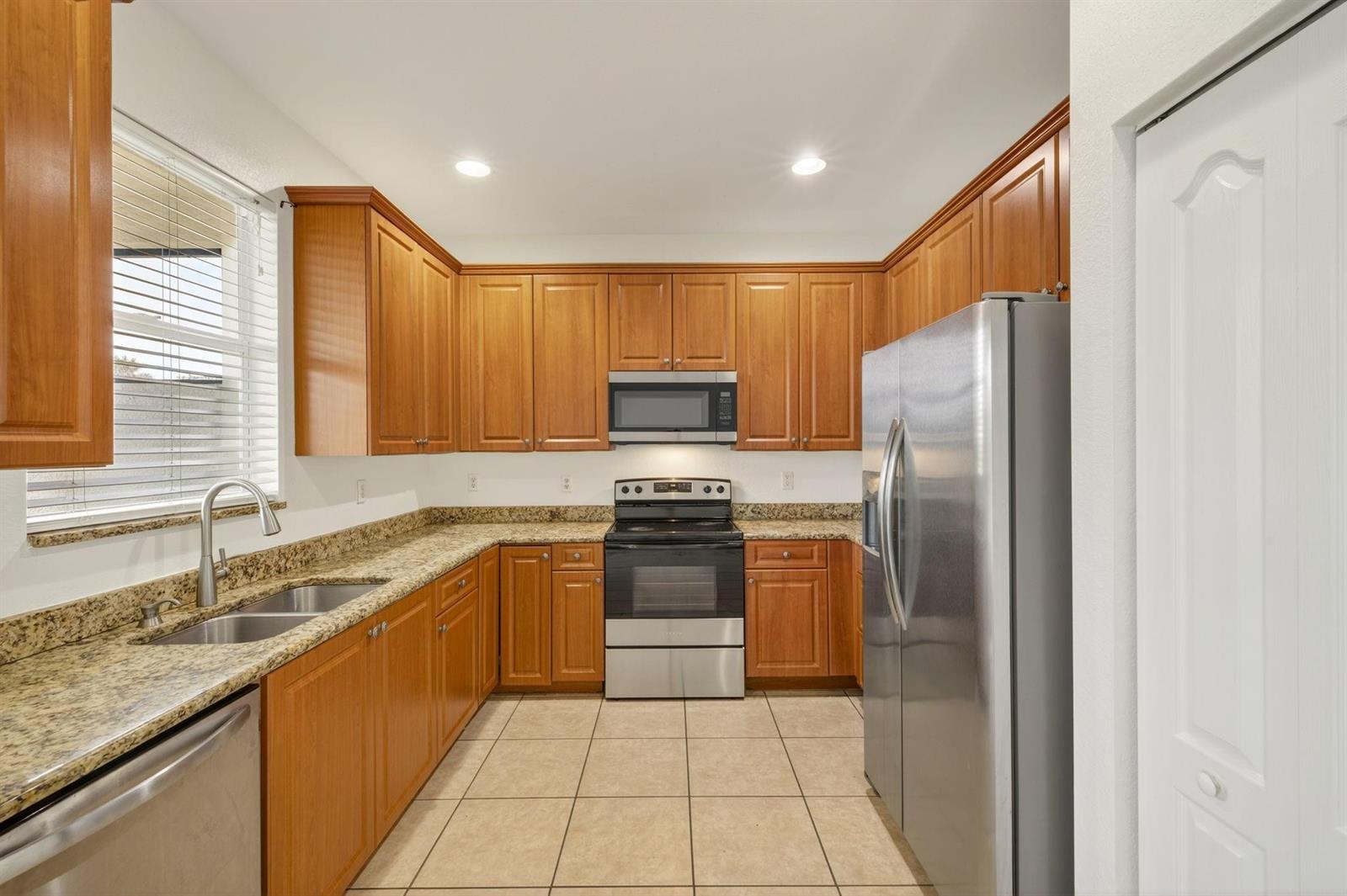A kitchen features wood cabinets, granite countertops, stainless steel appliances, and beige tile flooring — 7029 Ambrosia Lane # 606, Naples FL 34119, NAPLES, FL