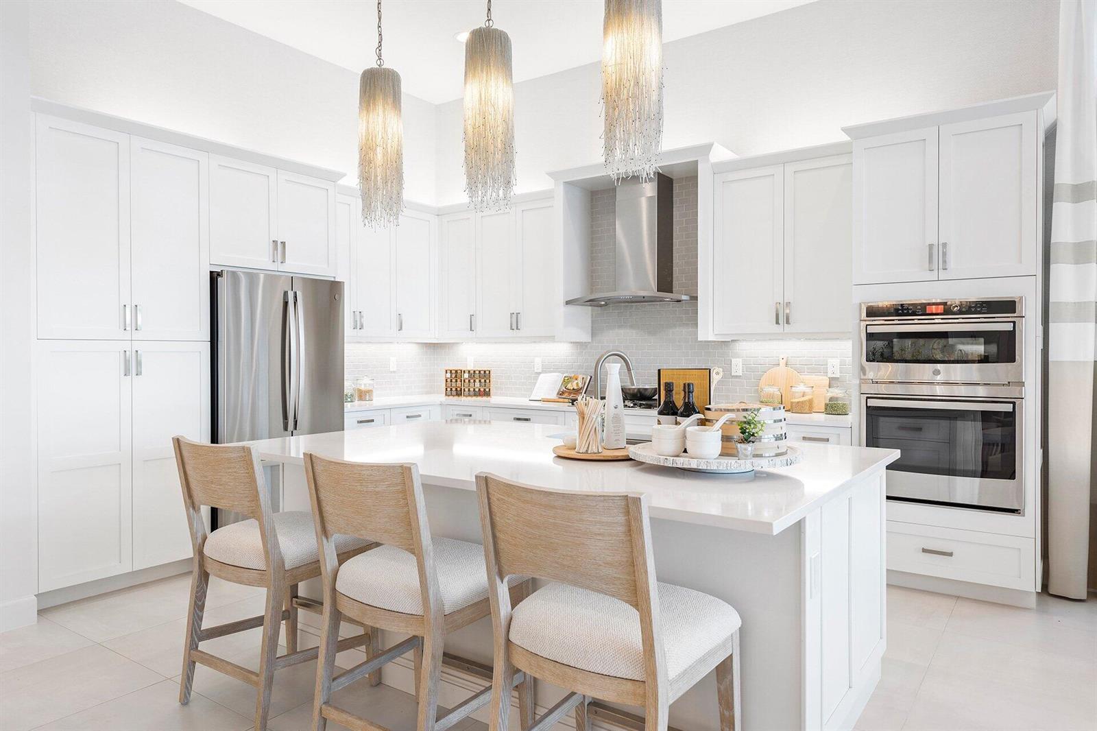 A modern white kitchen features a large island, stainless steel appliances, and three hanging lights — 9374 Mountain Pne Grove, Boynton Beach FL 33473, BOYNTON BEACH, FL