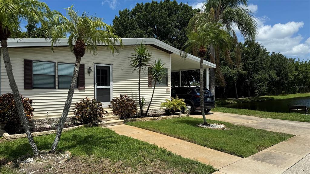 A light-colored mobile home features a carport, a front walkway, and palm trees — 1001 STARKEY ROAD UNIT 350, LARGO, FL