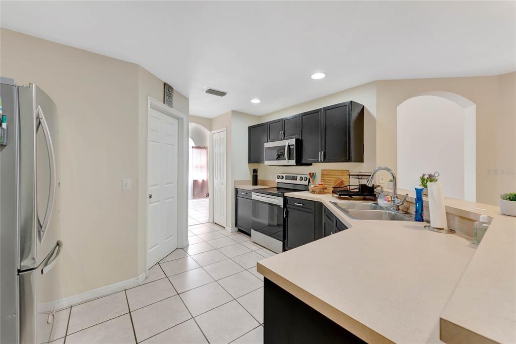 A kitchen features dark cabinets, stainless steel appliances, a light countertop, and white tile flooring — 68 HERRING COURT, KISSIMMEE, FL