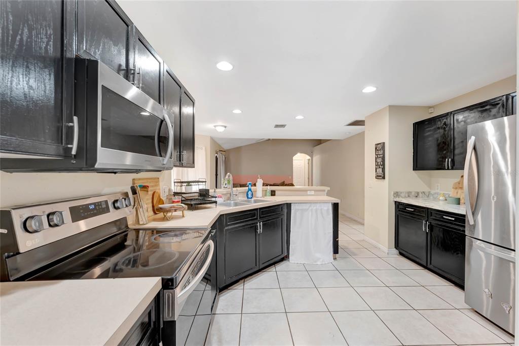 A kitchen features black cabinets, stainless steel appliances, and light-colored tile flooring — 68 HERRING COURT, KISSIMMEE, FL