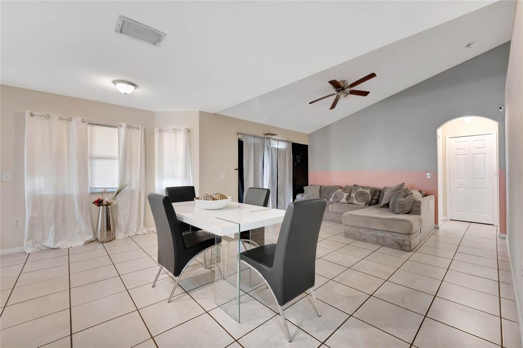 A dining area with a white table and black chairs sits before a living room — 68 HERRING COURT, KISSIMMEE, FL