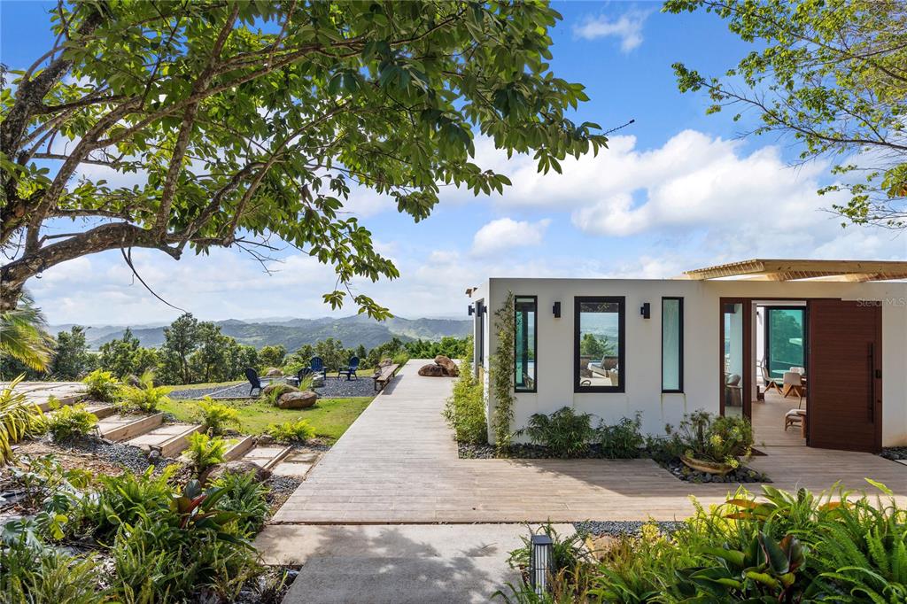 A modern house with a wooden deck overlooks a scenic mountain landscape under a blue sky — 24-2 Bo. Pena Pobre KM 2.3 VISTA DEL ESTE, NAGUABO, PR