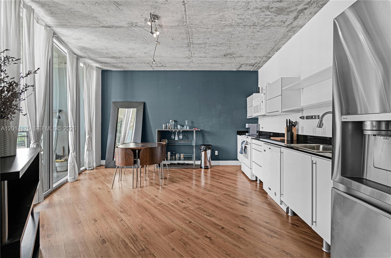 This open-concept kitchen and dining area features a concrete ceiling, wood flooring, and blue wall — 690 SW 1st Ct # 1934, Miami FL 33130, MIAMI, FL
