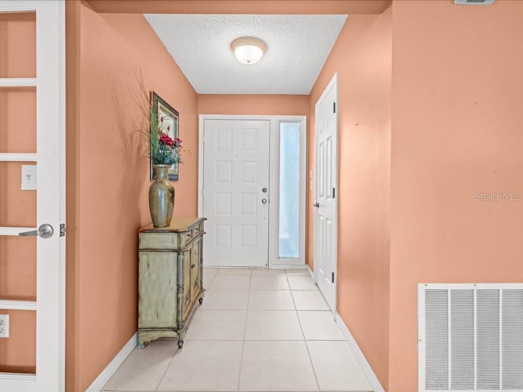 An entryway features peach-colored walls, a white front door, and a small wooden cabinet — 411 CYPRESS FOREST DRIVE, ENGLEWOOD, FL