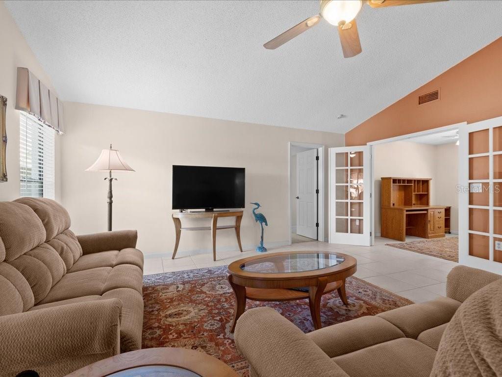 A living room features a beige sofa, a glass-top coffee table, and French doors — 411 CYPRESS FOREST DRIVE, ENGLEWOOD, FL