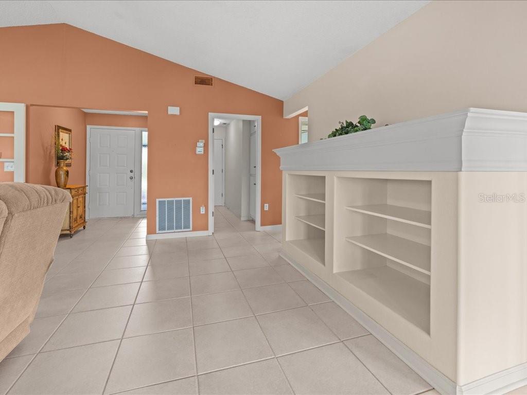 A living room features light tile floors, a built-in bookshelf, and a vaulted ceiling — 411 CYPRESS FOREST DRIVE, ENGLEWOOD, FL