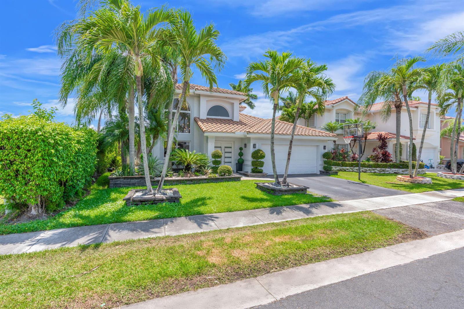 A two-story suburban house with a tiled roof, palm trees, and a basketball hoop — 52 Gables Boulevard, Weston FL 33326, WESTON, FL