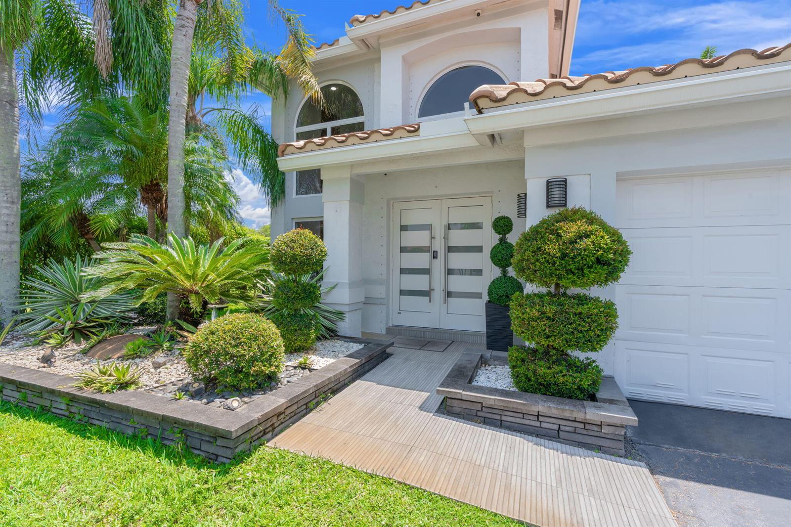 A two-story house exterior features a white double front door, tiled walkway, and manicured landscaping — 52 Gables Boulevard, Weston FL 33326, WESTON, FL
