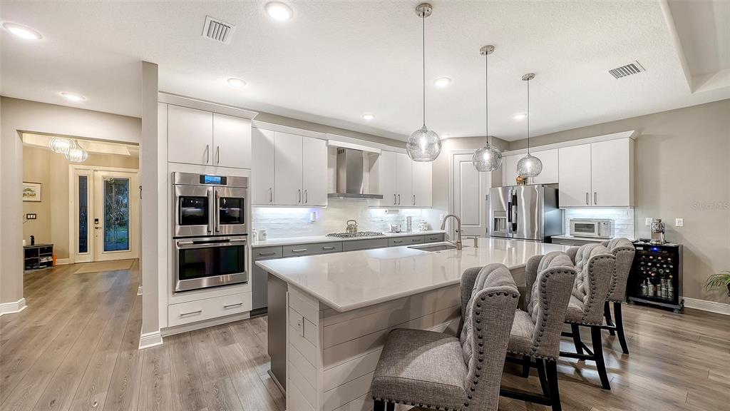 A modern kitchen features white cabinetry, a large island with gray chairs, and stainless appliances — 4921 SURFSIDE CIRCLE, BRADENTON, FL