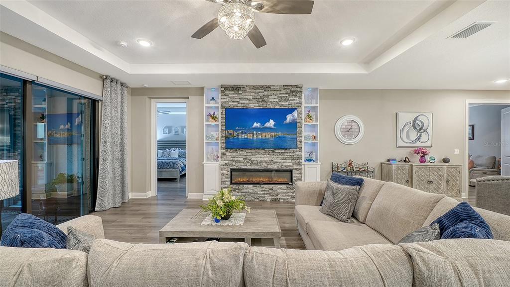 A living room features a stone fireplace, built-in shelving, a sectional sofa, and wood flooring — 4921 SURFSIDE CIRCLE, BRADENTON, FL