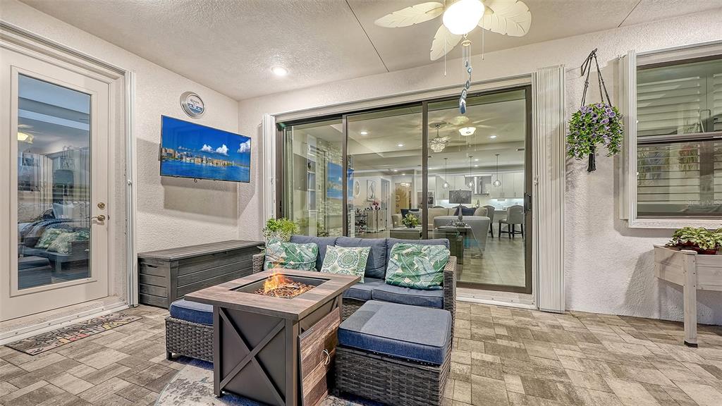A covered patio features a fire pit, outdoor sofa, wall-mounted television, and sliding glass doors — 4921 SURFSIDE CIRCLE, BRADENTON, FL