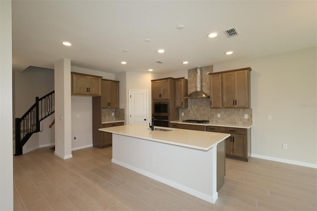A modern kitchen features wood cabinets, a large white island, and light-colored tile flooring — 1314 HYDE STREET, ST CLOUD, FL