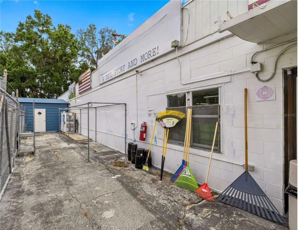 An exterior view of a white concrete block building with rakes leaning against the wall — 2926/3010 NE JACKSONVILLE ROAD, OCALA, FL