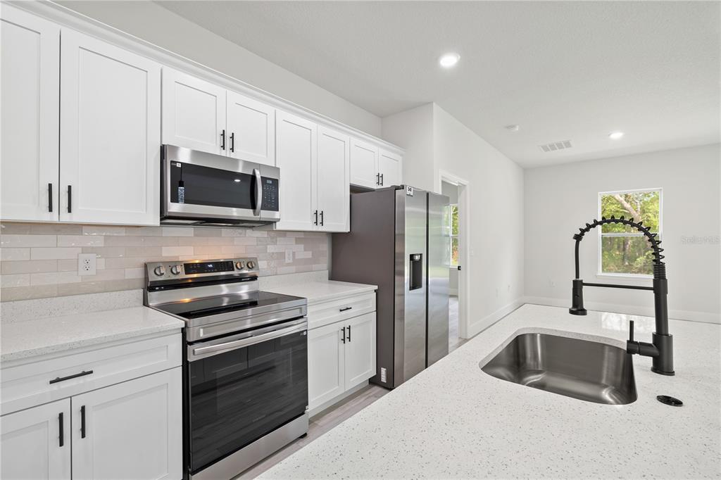 A modern kitchen features white cabinets, stainless steel appliances, quartz countertops, and a large island — 1978 W RUTLAND DRIVE, CITRUS SPRINGS, FL