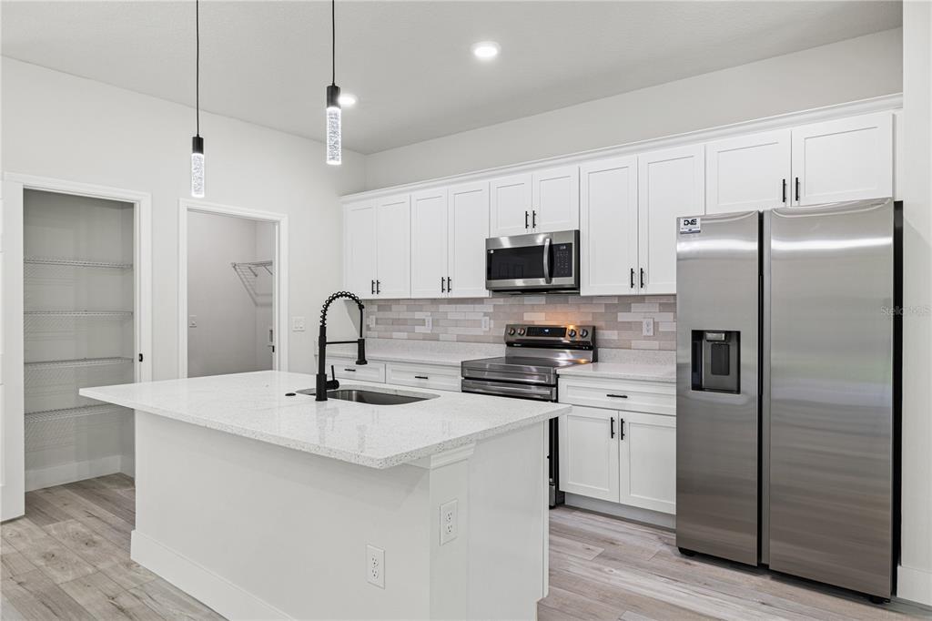 A modern kitchen features white cabinets, stainless steel appliances, a quartz island, and wood-look flooring — 1978 W RUTLAND DRIVE, CITRUS SPRINGS, FL