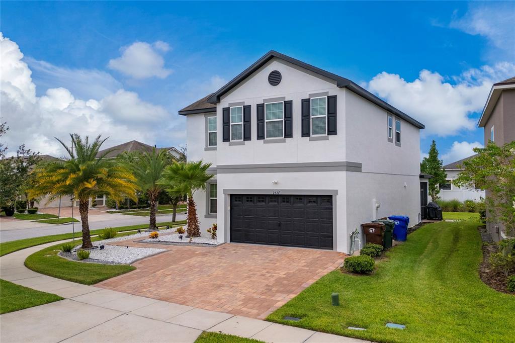 A two-story white house with a black garage door and a brick paver driveway — 2527 NOUVEAU WAY, KISSIMMEE, FL