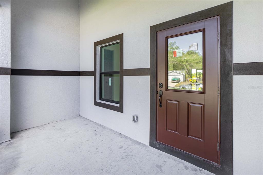 A covered concrete porch features a brown front door with a glass pane and window — 7316 DONAHUE STREET, PORT CHARLOTTE, FL