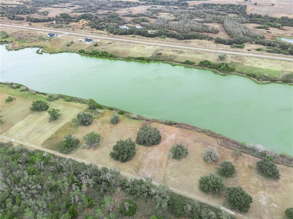An aerial view shows a large green pond bordered by a dirt road and trees — 10349 COUNTY ROAD 555, FORT MEADE, FL