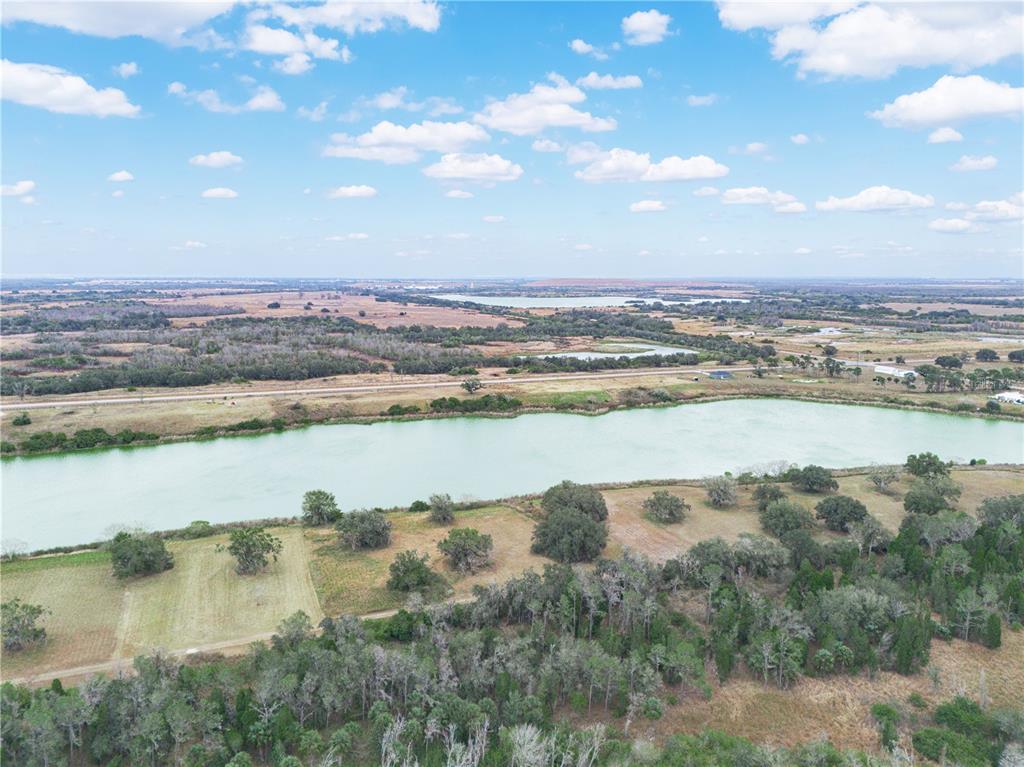 An aerial view shows a large pond surrounded by grassy fields, trees, and a distant road — 10349 COUNTY ROAD 555, FORT MEADE, FL