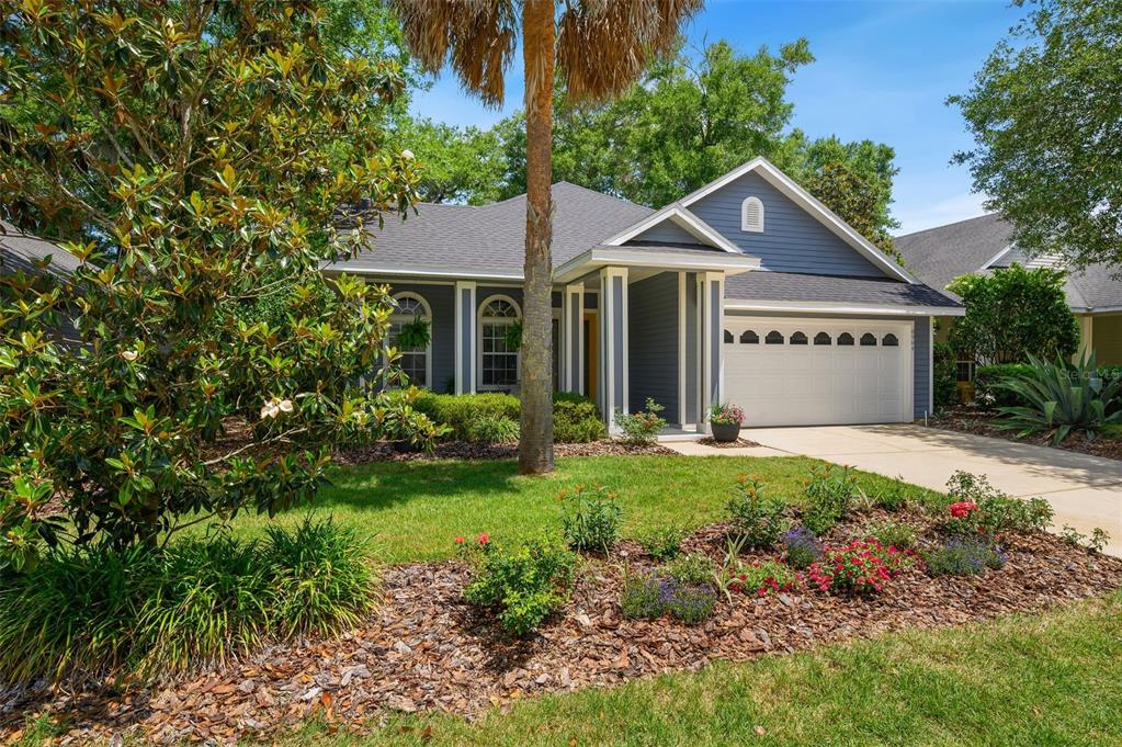 A blue single-story house with a white garage door and a front yard garden — 8964 SW 64TH LANE, GAINESVILLE, FL