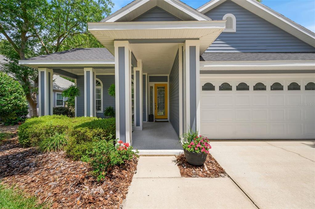 A blue house exterior features a covered entryway with a yellow front door and garage — 8964 SW 64TH LANE, GAINESVILLE, FL