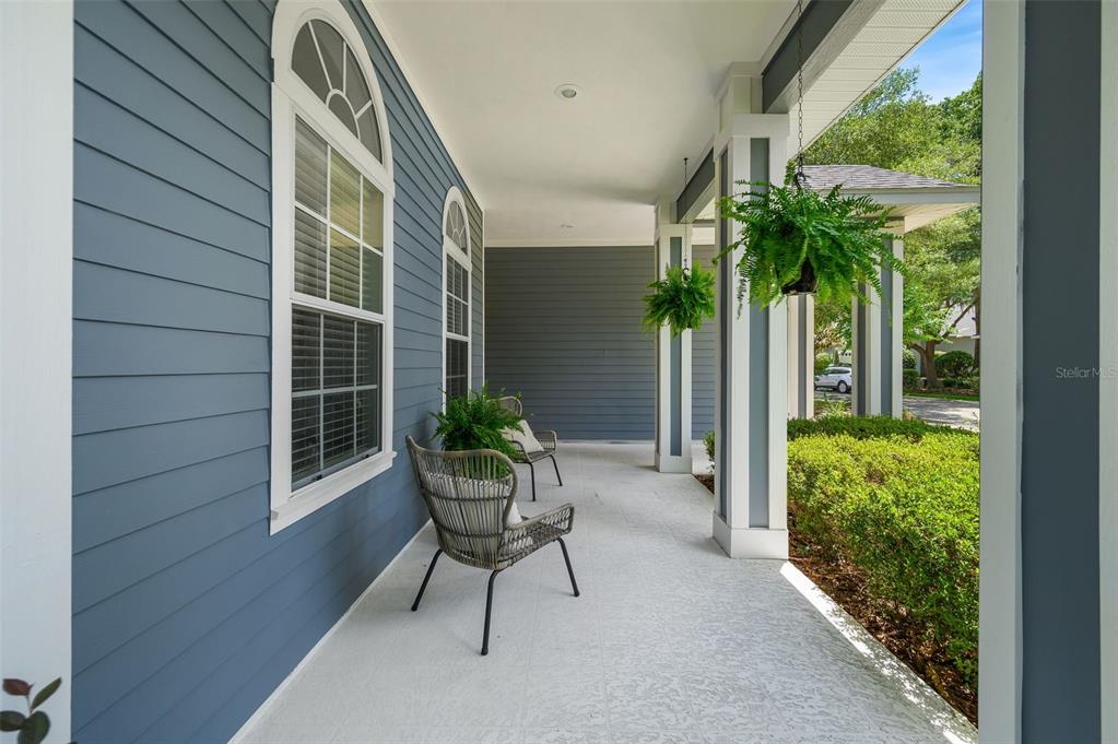 A covered front porch features blue horizontal siding, white columns, and two wicker chairs — 8964 SW 64TH LANE, GAINESVILLE, FL