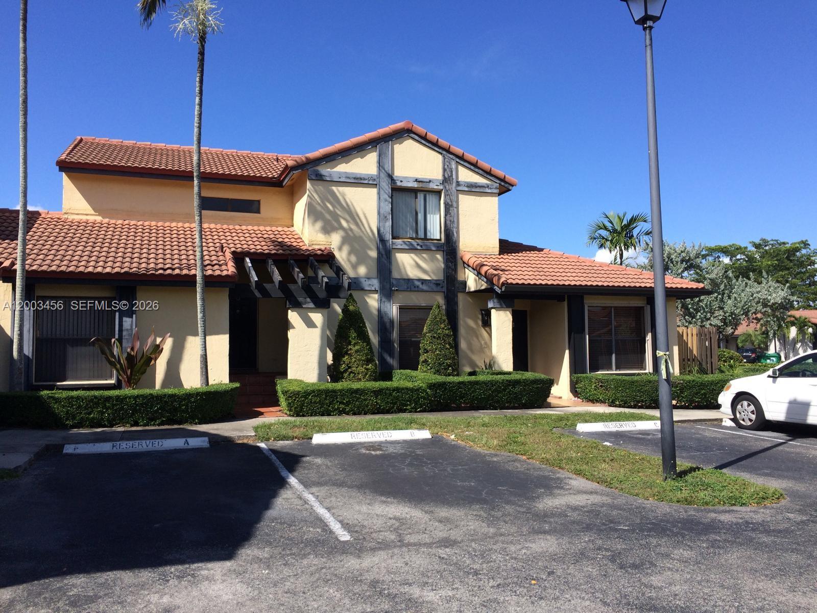 A two-story stucco building with a tiled roof features reserved parking spaces in front — 15070 SW 49th Ln # D106, Miami FL 33185, MIAMI, FL