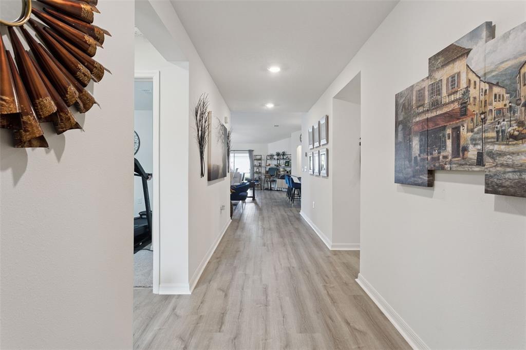 A hallway with light wood-look flooring leads toward an open-concept living area — 3832 PRONGHORN DR, ST CLOUD, FL