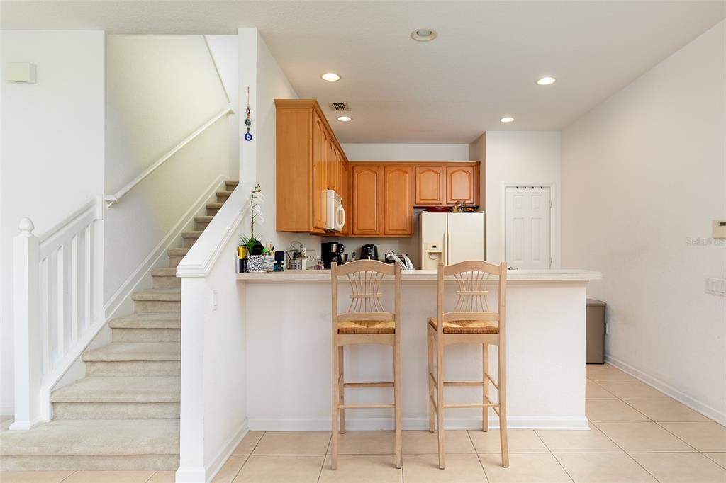 A kitchen features wooden cabinets, a breakfast bar with two chairs, and an adjacent staircase — 1173 SHALLCROSS AVENUE, ORLANDO, FL