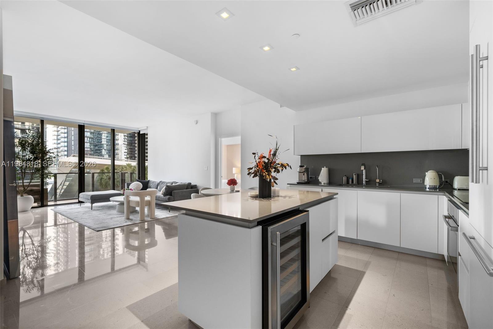 A modern kitchen with a central island and wine cooler opens into a bright living area — 88 SW 7th St # 809, Miami FL 33130, MIAMI, FL