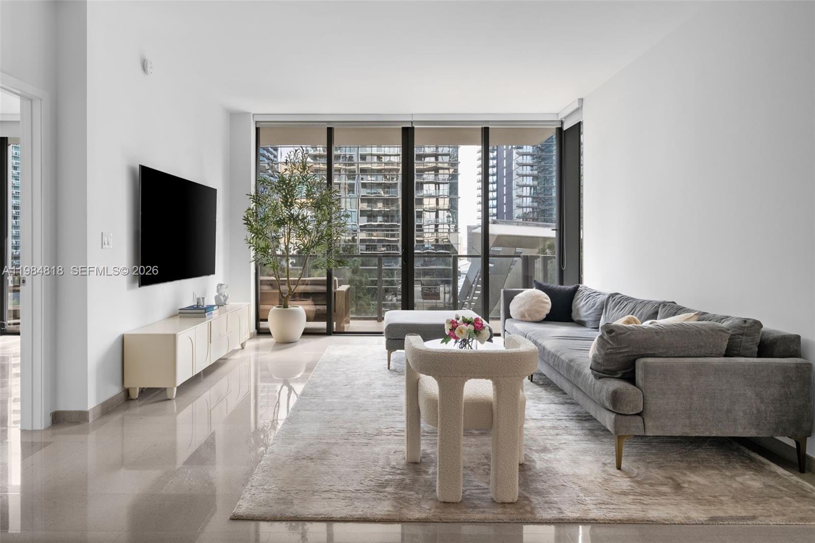 A modern living room features a gray sofa, a white coffee table, and floor-to-ceiling windows — 88 SW 7th St # 809, Miami FL 33130, MIAMI, FL