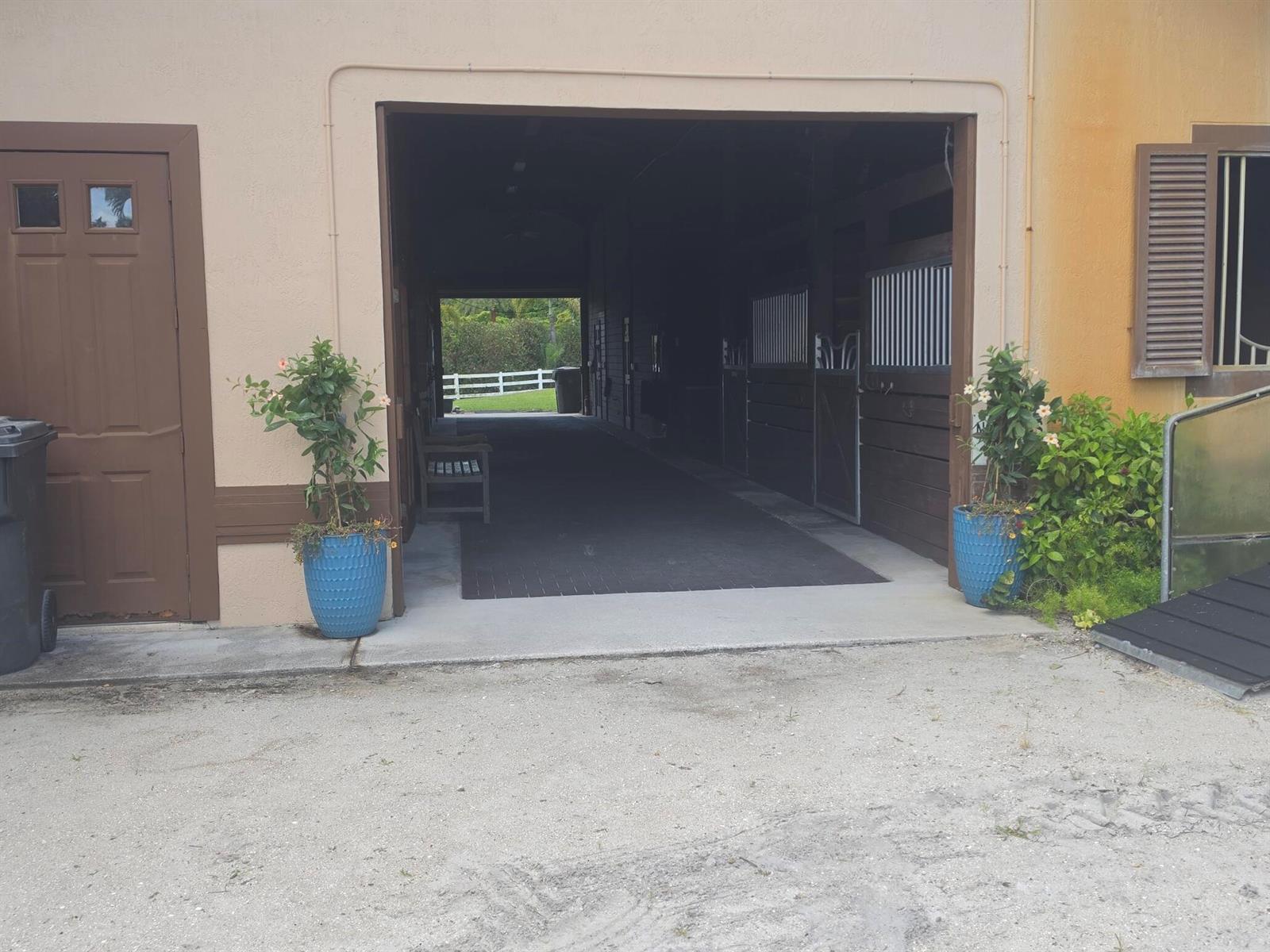 A view of a horse barn aisle with stalls, flanked by two blue potted plants — 14127 Equestrian Way, Wellington FL 33414, WELLINGTON, FL