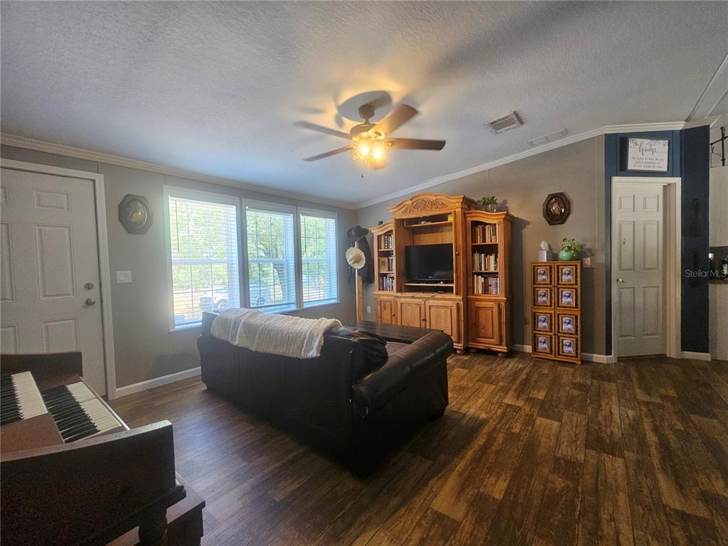 A living room features wood-look flooring, a leather sofa, a wooden entertainment center, and piano — 9172 QUIVIRA ROAD, BROOKSVILLE, FL