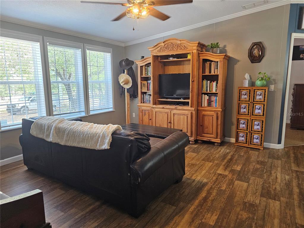 A living room features a dark leather sofa, wood-toned entertainment center, and wood-look flooring — 9172 QUIVIRA ROAD, BROOKSVILLE, FL
