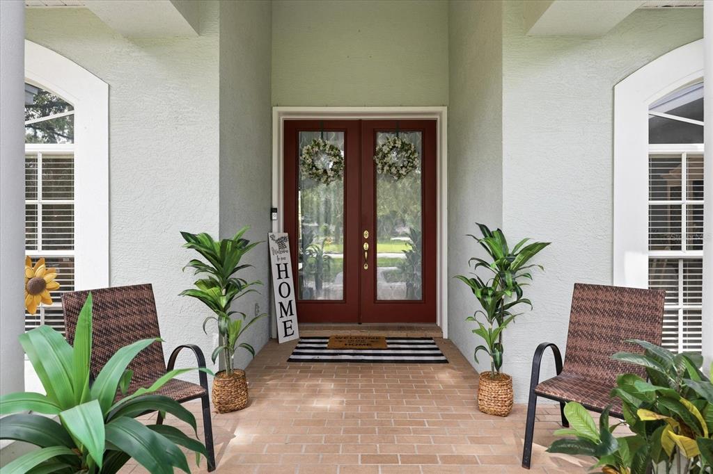 A covered front porch features a red double door, two chairs, and potted plants — 6636 ROYAL FOREST DRIVE, LAKELAND, FL