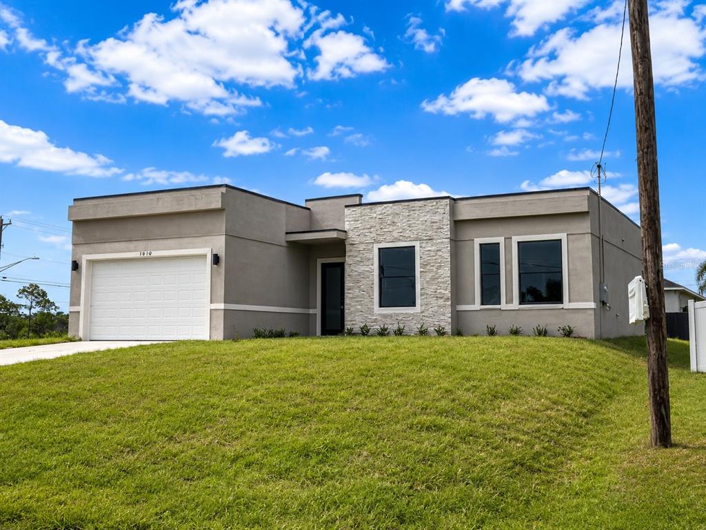 A modern single-story house with a beige stucco exterior, stone accent wall, and white garage — 1610 NE 34TH STREET, CAPE CORAL, FL