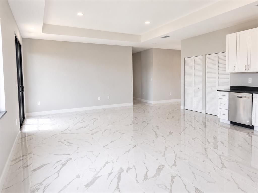 A bright living area with white marble-look tile flooring and an adjacent kitchen with cabinets — 1610 NE 34TH STREET, CAPE CORAL, FL