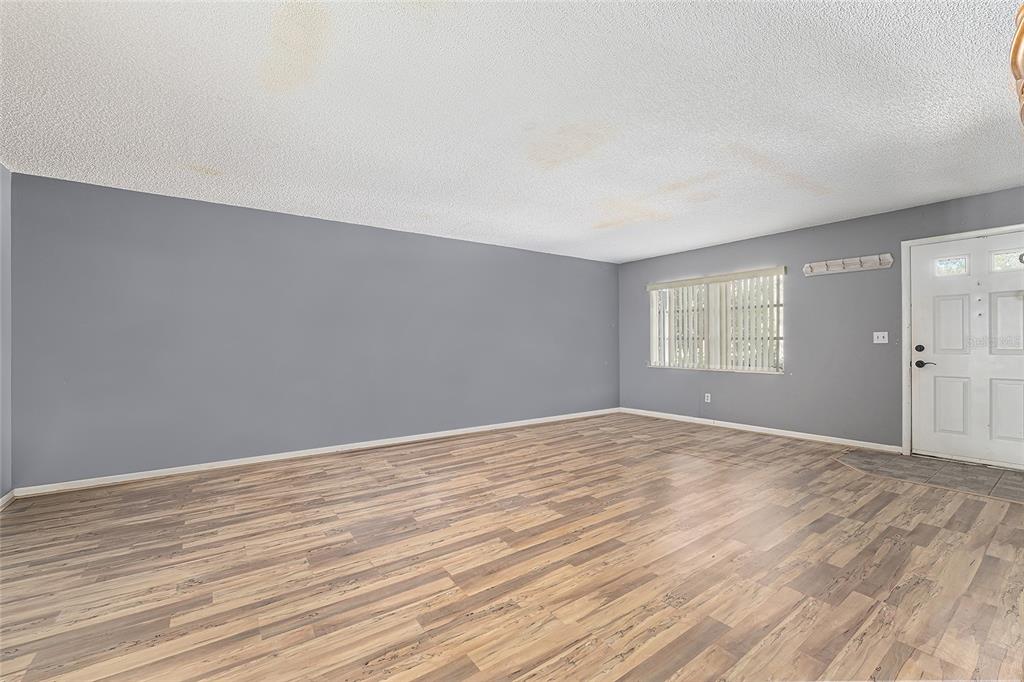 An empty living room features gray walls, wood-look flooring, and a textured white ceiling — 9951 SW 88TH COURT ROAD UNIT C, OCALA, FL