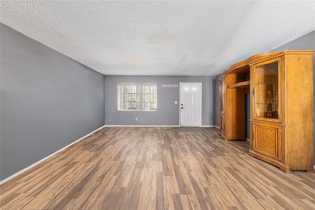 An empty living room features gray walls, wood-look flooring, a window, and a large cabinet — 9951 SW 88TH COURT ROAD UNIT C, OCALA, FL