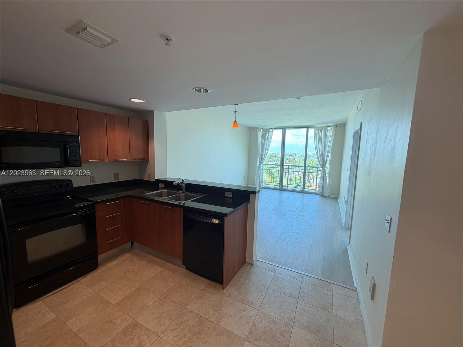 A kitchen with wood cabinets and black appliances opens to a living area with balcony views — 2021 SW 3rd Ave # 902, Miami FL 33129, MIAMI, FL