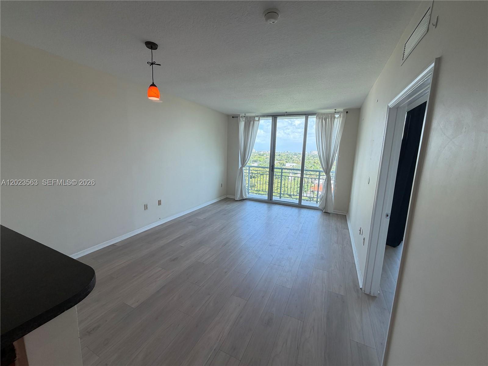 An empty living room features light wood-look flooring, a pendant light, and a balcony view — 2021 SW 3rd Ave # 902, Miami FL 33129, MIAMI, FL