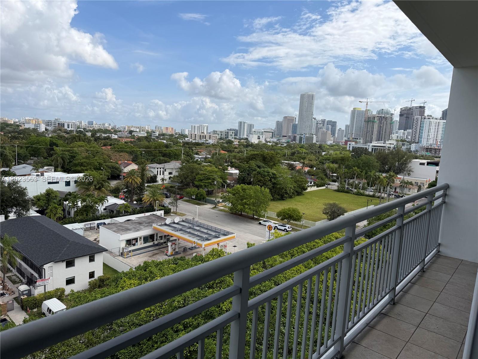 A high-angle view from a balcony overlooks a gas station, surrounding trees, and a city skyline — 2021 SW 3rd Ave # 902, Miami FL 33129, MIAMI, FL