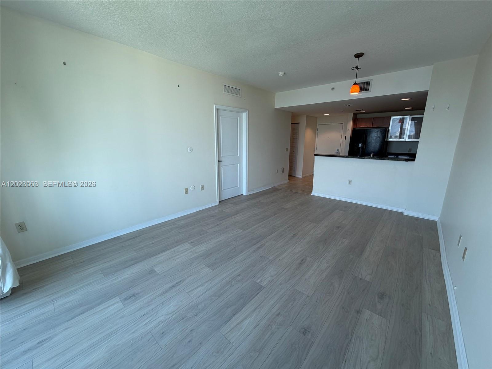 An empty living area features light wood-look flooring, white walls, and an open kitchen — 2021 SW 3rd Ave # 902, Miami FL 33129, MIAMI, FL